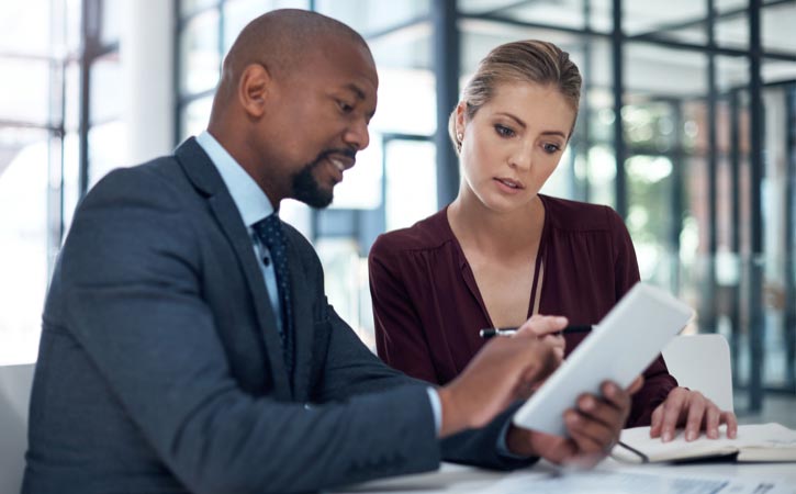 Un homme et une femme d’affaires regardent une tablette numérique dans un bureau d’allure moderne.