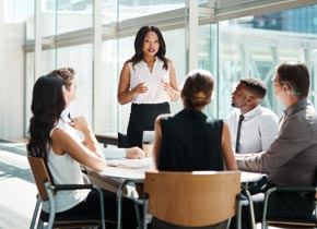 Professional group in a meeting setting with female speaker standing