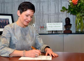 Penny Pennington, Managing Partner, signing a document while sitting at a desk.