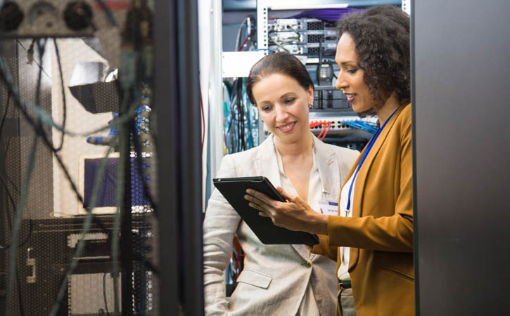 Women in data center programing mainframe through digital tablet.
