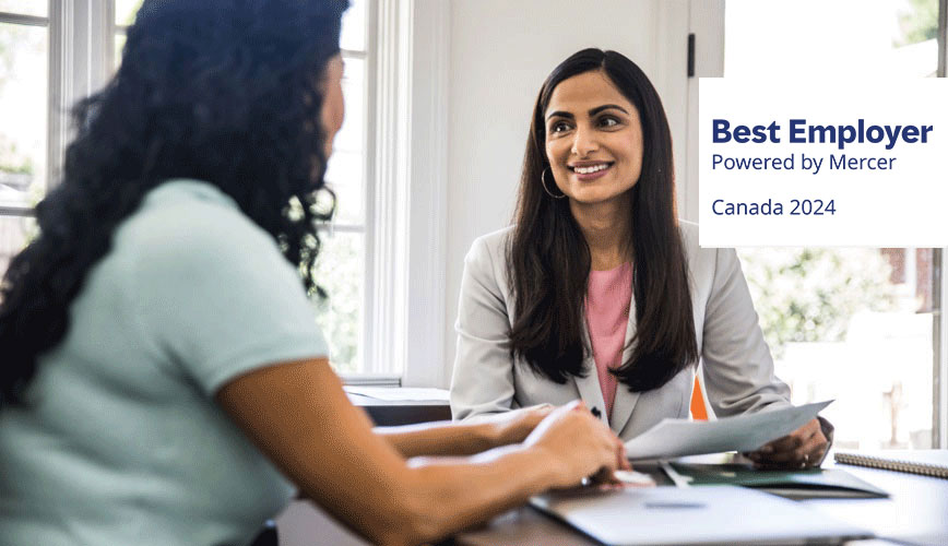 Two women having a discussions with Canada Best Employer By Mercer Logo