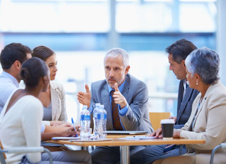 Small group meeting of professionals listening to one male speak.