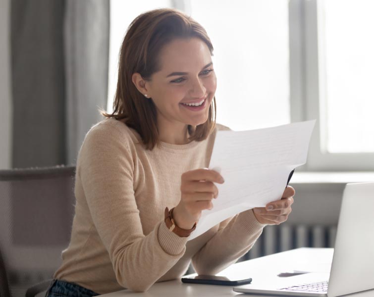 A smiling woman looking at paperwork at her desk.