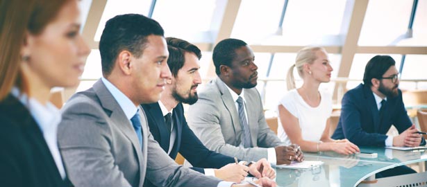 Group of professionals sitting at a conference table, listening.