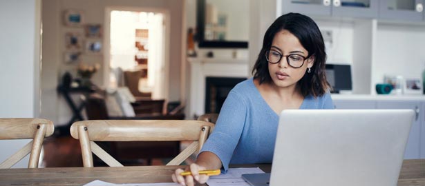 Female working from home at dining room table on laptop.