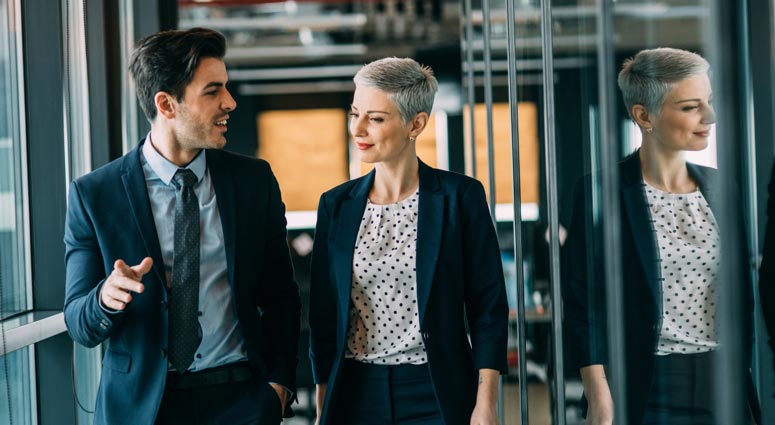A man and woman walking down an office corridor.