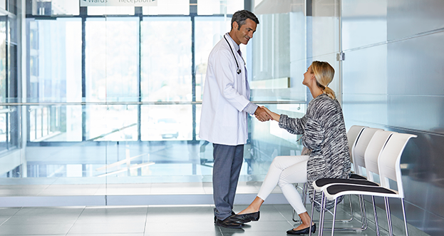 Male doctor speaking and shaking hand with a female patient, while she is sitting down.