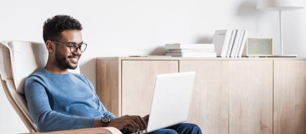 Un homme est assis sur une chaise et travaille de chez lui sur un ordinateur portable.